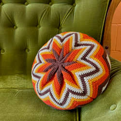 Colorful crocheted round pillow on a green cushioned chair.