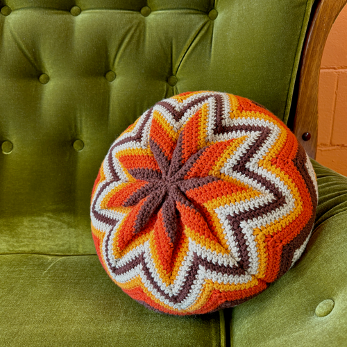 Colorful crocheted round pillow on a green cushioned chair.